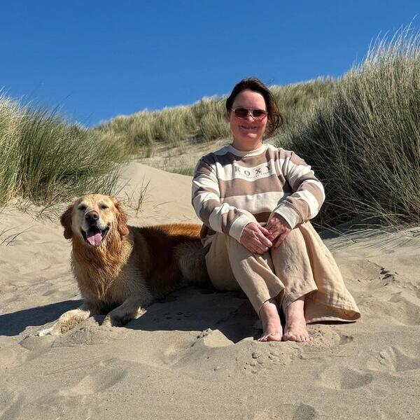 Die Freie Rednerin Silke Lentz sitz mit ihrem Golden Retriever am Strand.
